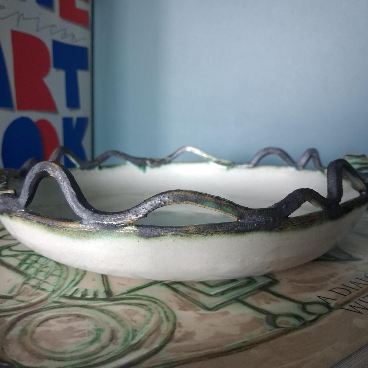 A decorative studio pottery shallow glazed bowl with fish and wave detailed rim
