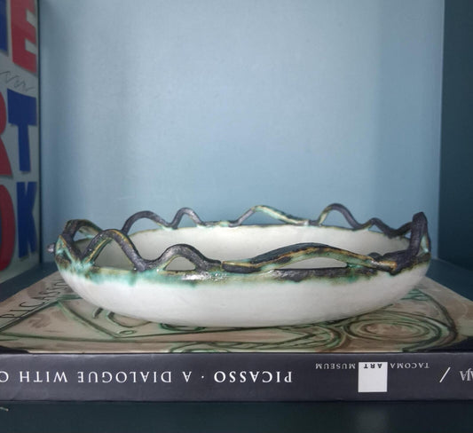 A decorative studio pottery shallow glazed bowl with fish and wave detailed rim