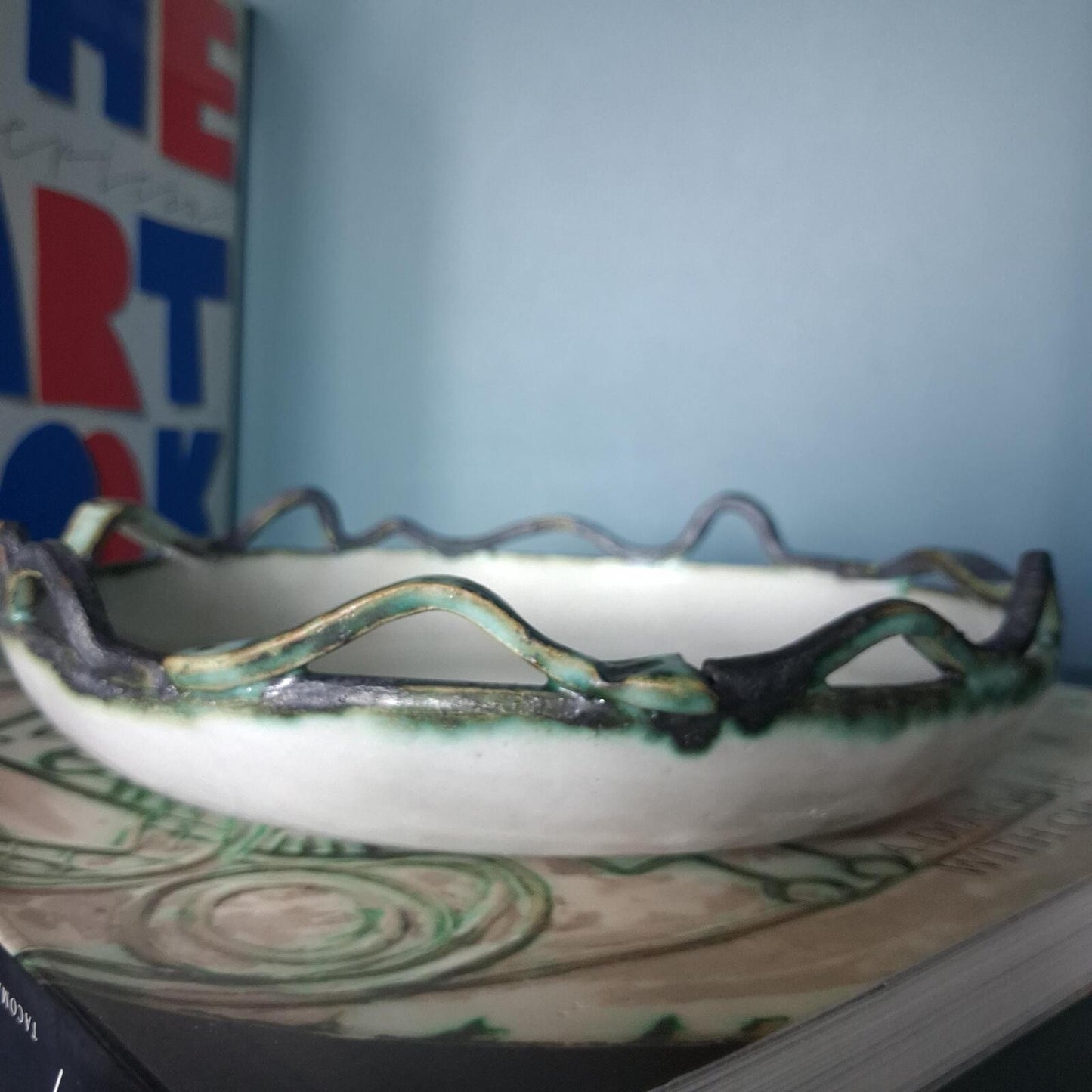 A decorative studio pottery shallow glazed bowl with fish and wave detailed rim