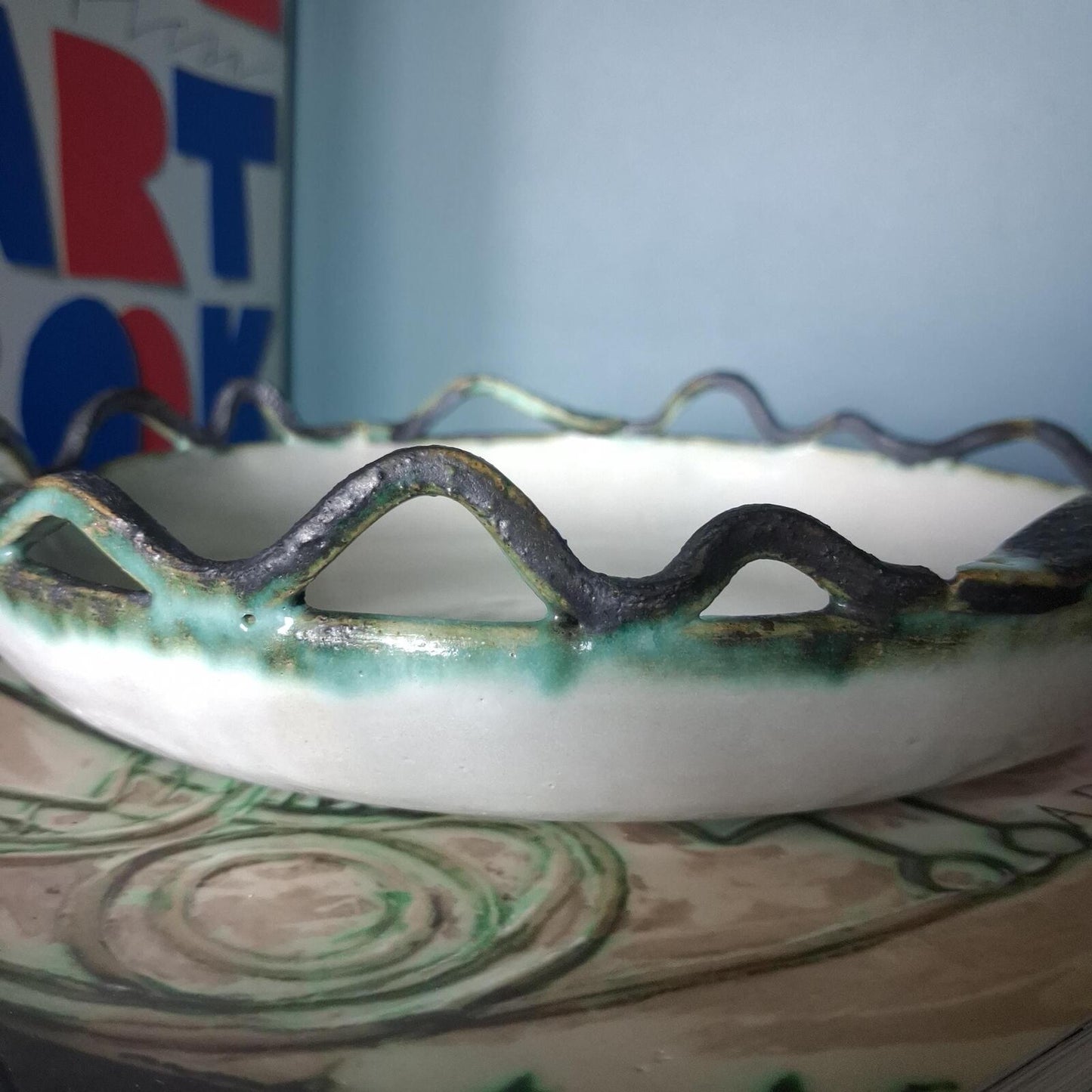 A decorative studio pottery shallow glazed bowl with fish and wave detailed rim