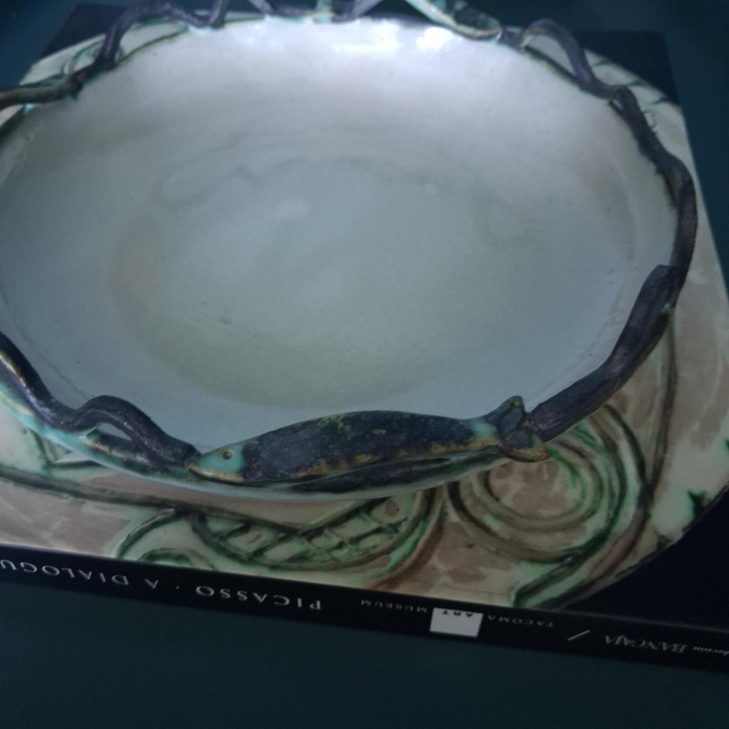 A decorative studio pottery shallow glazed bowl with fish and wave detailed rim